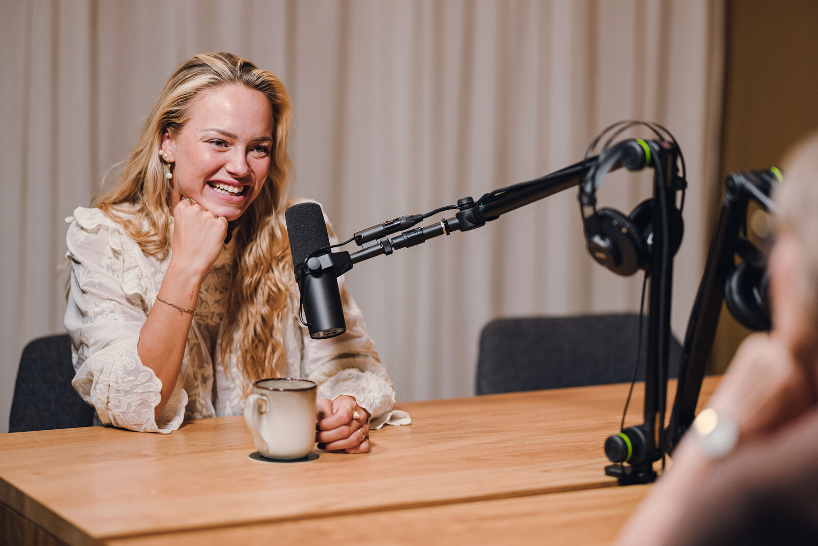 Kvinde griner ved mikrofonen midt i sin egen podcastoptagelse